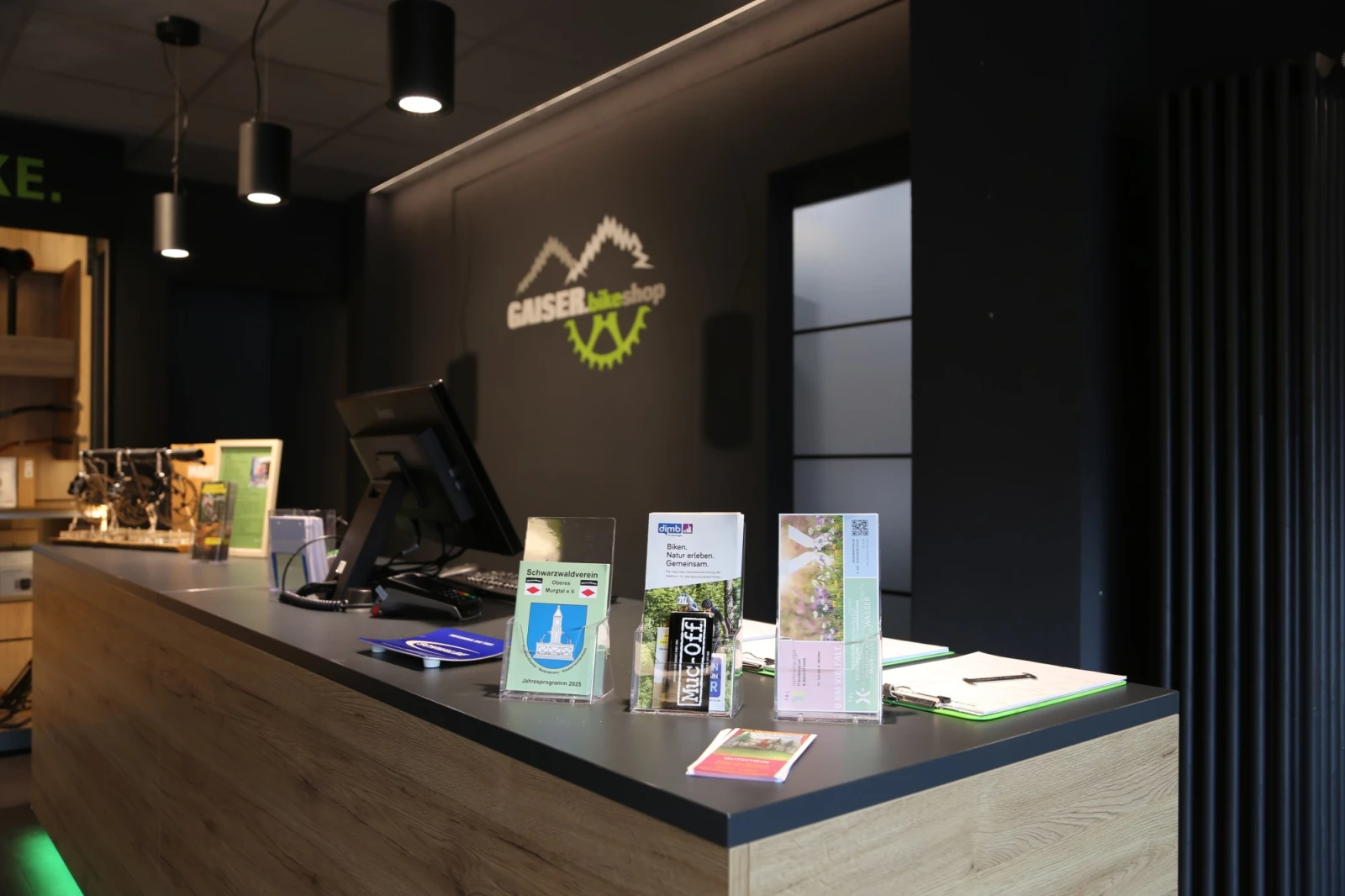 Empfangstheke des Gaiser bikeshop mit Logo an der Wand und Informationsmaterialien auf der Theke.