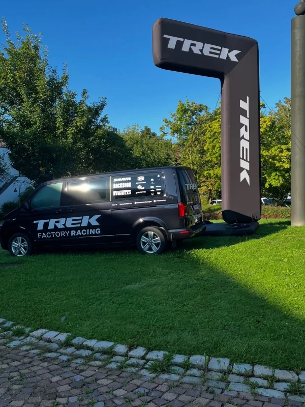Trek Factory Racing Fahrzeug neben gro&szlig;em Trek-Logo auf gr&uuml;ner Wiese.