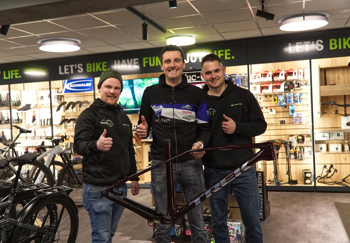 Drei M&auml;nner halten ein Mountainbike in einem Fahrradgesch&auml;ft und l&auml;cheln in die Kamera.