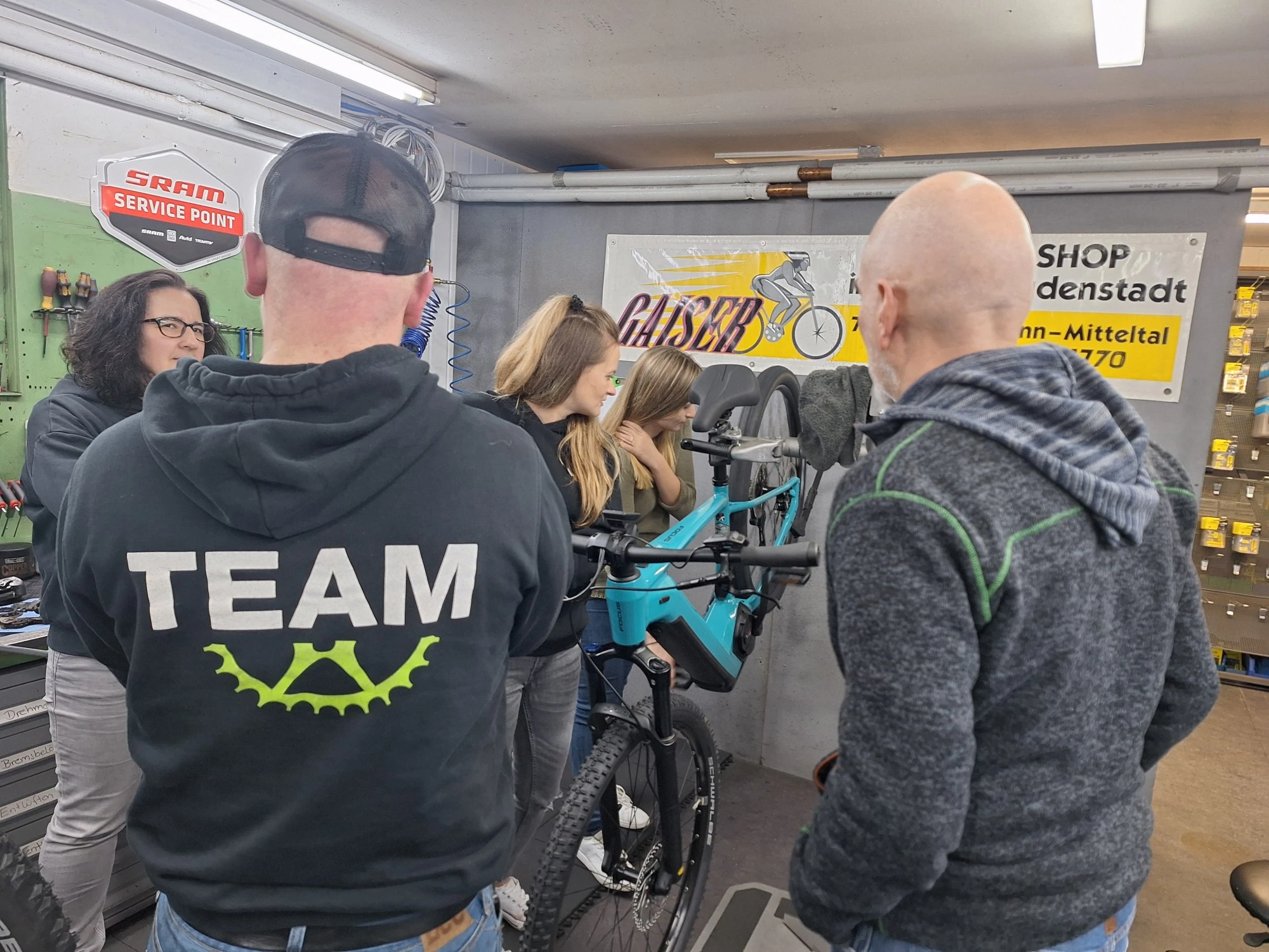 Mehrere Personen in einer Fahrradwerkstatt besprechen sich an einem Fahrrad.