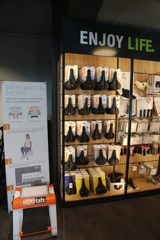 Schaufenster mit Fahrradsatteln in verschiedenen Farben und Gr&ouml;&szlig;en, daneben Infotafel zur Beratung.