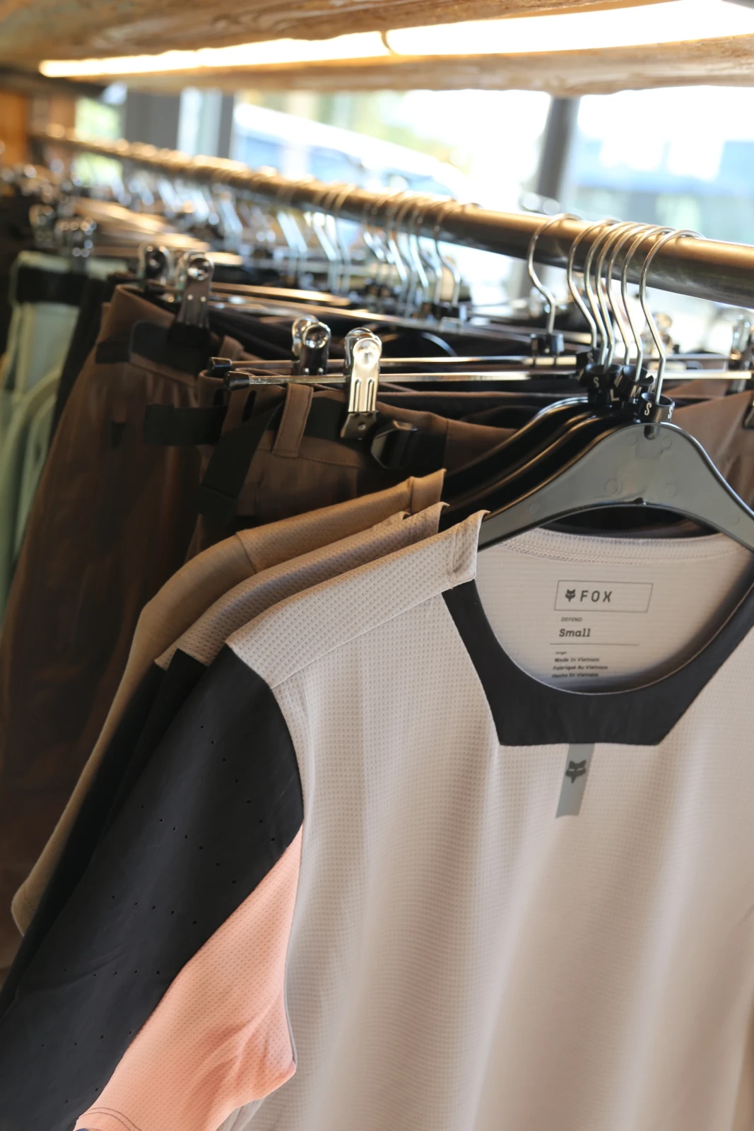 Kleidungsst&uuml;cke h&auml;ngen an einer Kleiderstange im Fahrradladen, darunter ein wei&szlig;es Shirt mit Etikett.