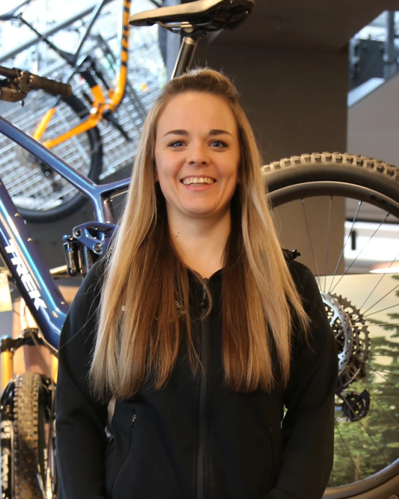Junge Frau mit langen braunen Haaren l&auml;chelt vor Fahrr&auml;dern im Bikeshop.