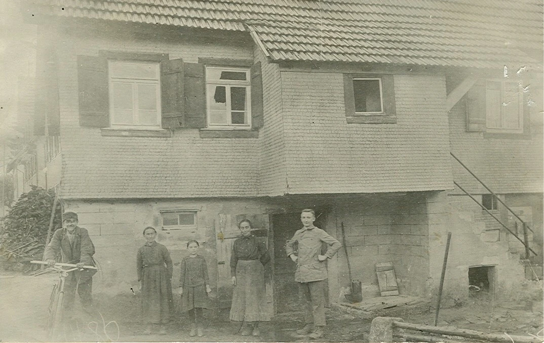 Historisches Schwarzwei&szlig;foto einer Familie vor einem Wohnhaus mit Unterstand.