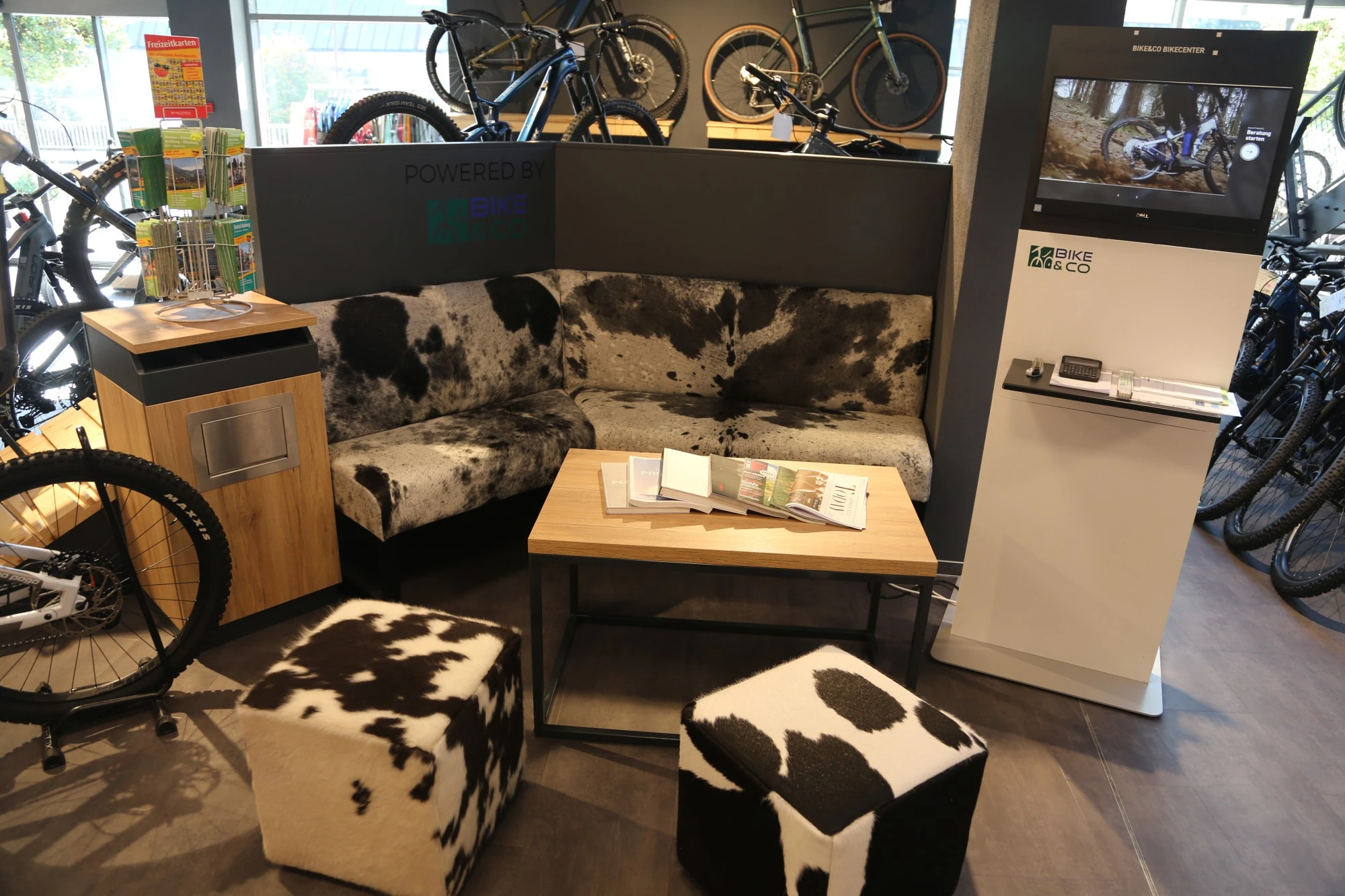 Sitzbereich im Gaiser Bikeshop mit Couch, Kuhfell-Poufs und Fahrr&auml;dern im Hintergrund.