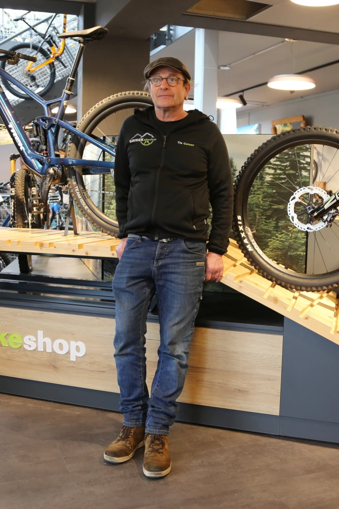 Mann mit Brille und Kappe im Gaiser-Bikeshop neben einem Fahrradreifen.