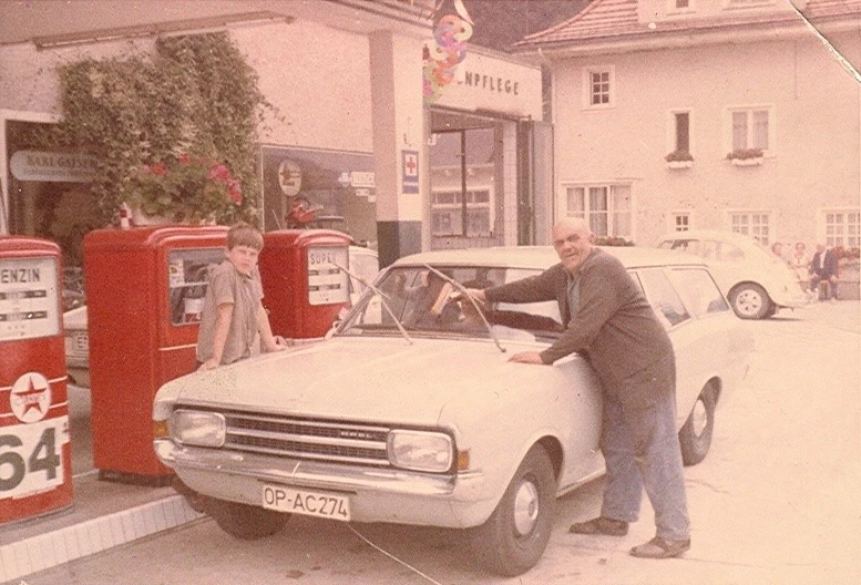 Mann tankt einen wei&szlig;en Opel an einer roten Zapfs&auml;ule in den 1980er Jahren.