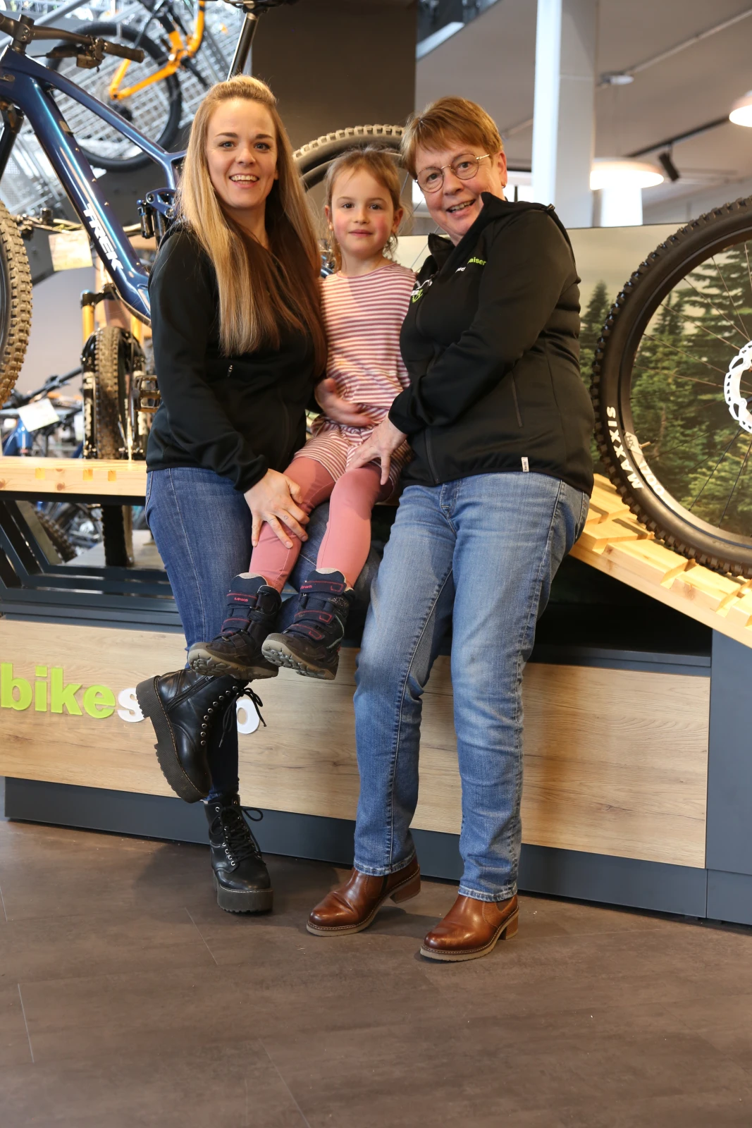 Zwei Frauen und ein Kind posieren vor Fahrr&auml;dern im Bikeshop.